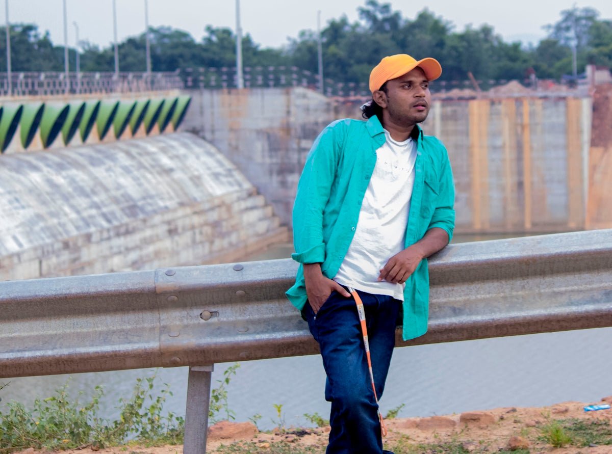 man in white dress shirt and blue denim jeans wearing yellow cap standing on brown wooden