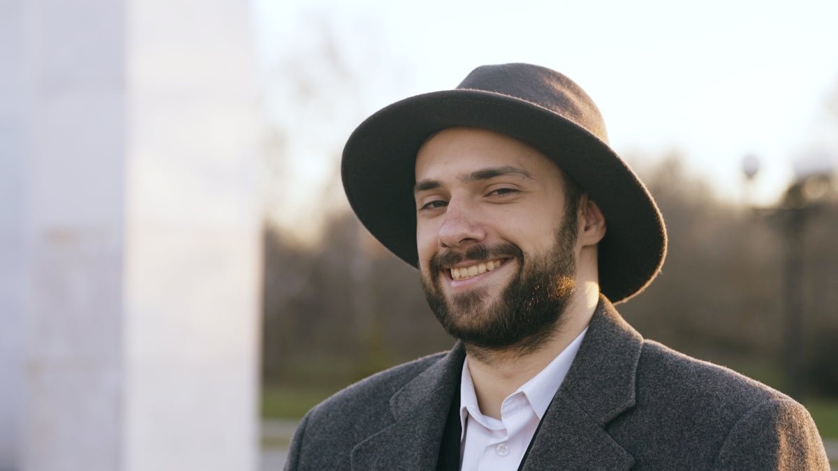A smiling man wearing a hat and coat outdoors