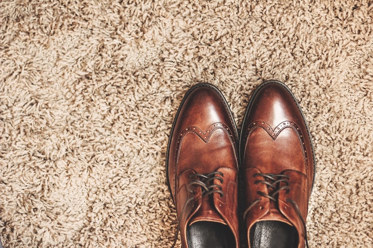 Brown leather dress shoes on a textured carpet