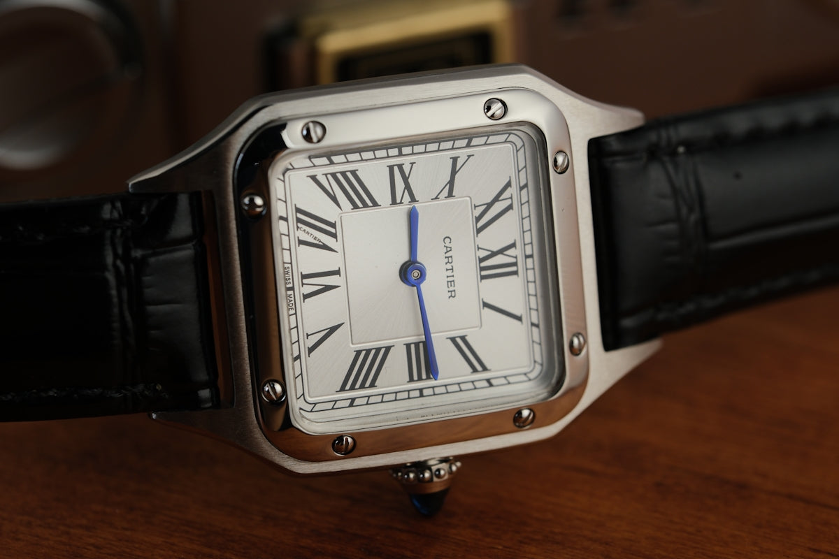 A silver square watch with a black leather strap.