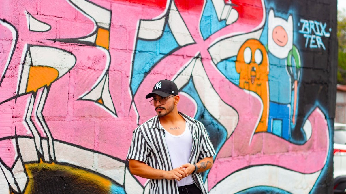 Man in striped shirt stands against graffiti wall