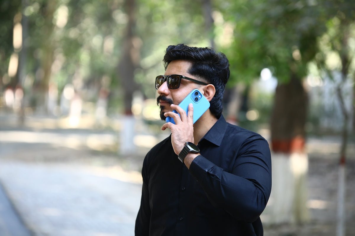 Man in black shirt talking on blue phone outdoors