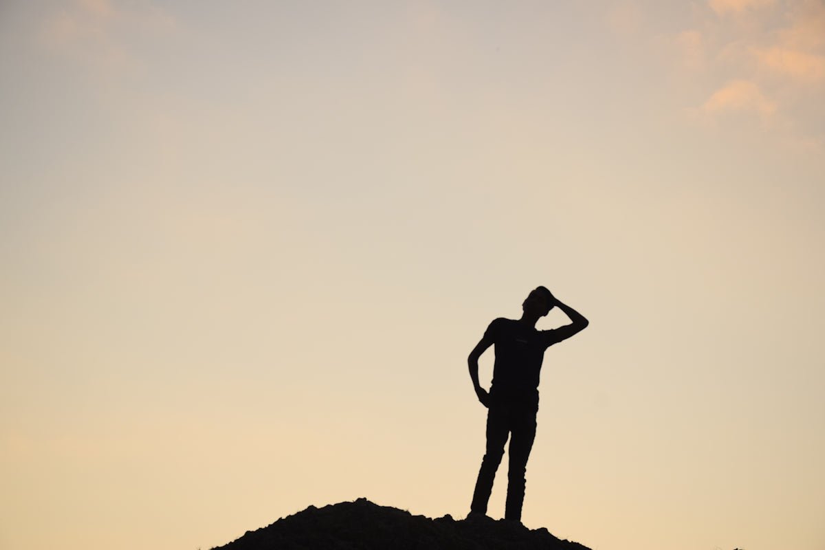 Silhouette of a person standing on a hill at sunset.