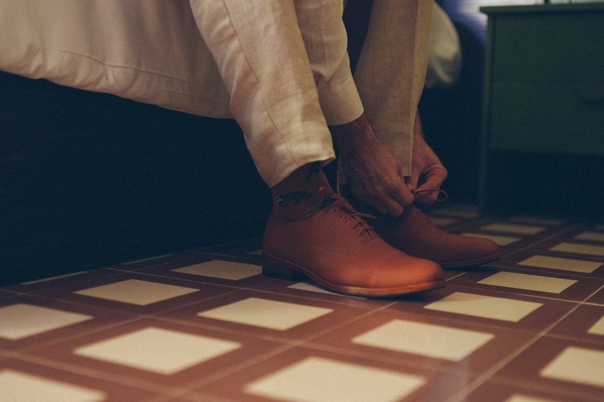 Person tying laces on brown leather shoes
