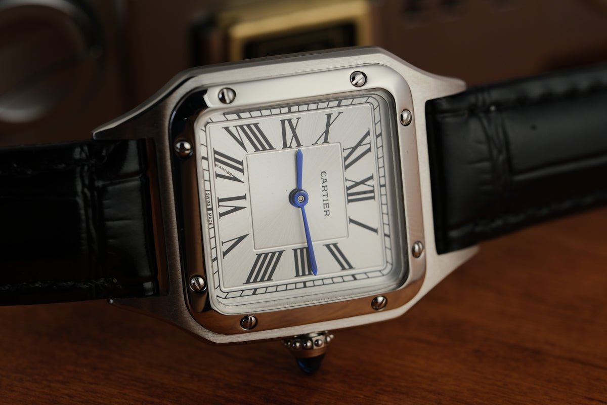 A silver square watch with a black leather strap.